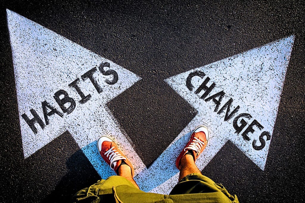 Wanting to lower healthcare costs, a person stands on two arrows pointing differen directions. One says "Habits" while the other says "Changes." To lower healthcare costs, many people must make change and leave old habits.