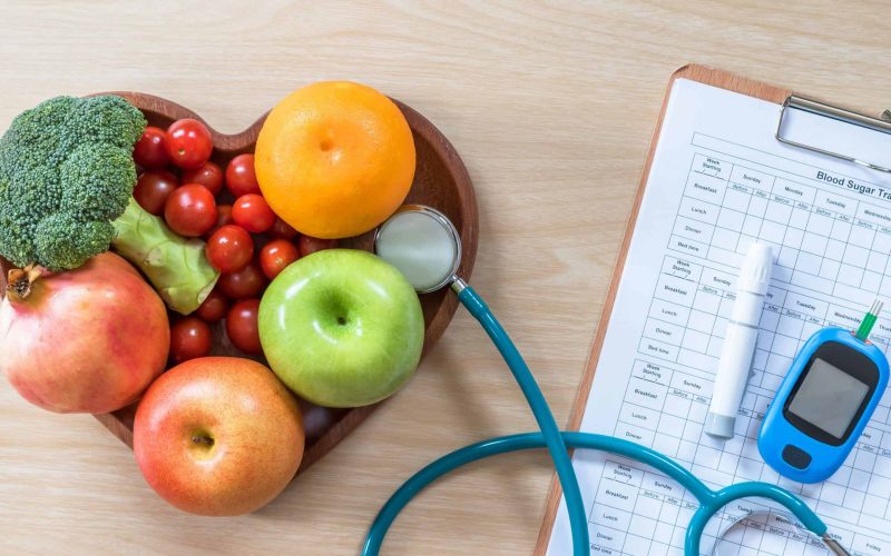 Diabetes monitor, Cholesterol diet and healthy food eating nutritional concept with clean fruits in nutritionist's heart dish and patient's  blood sugar control record with diabetic measuring tool kit