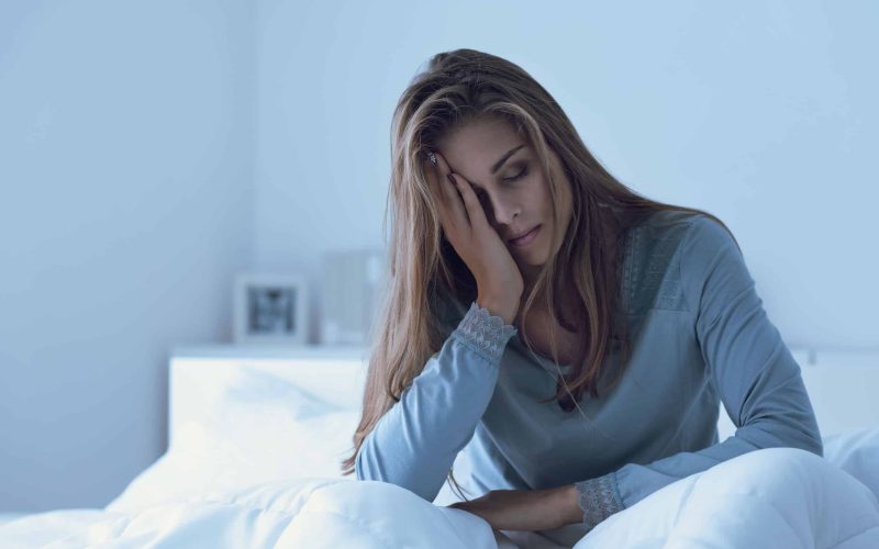 Depressed woman awake in the night, she is touching her forehead and suffering from insomnia