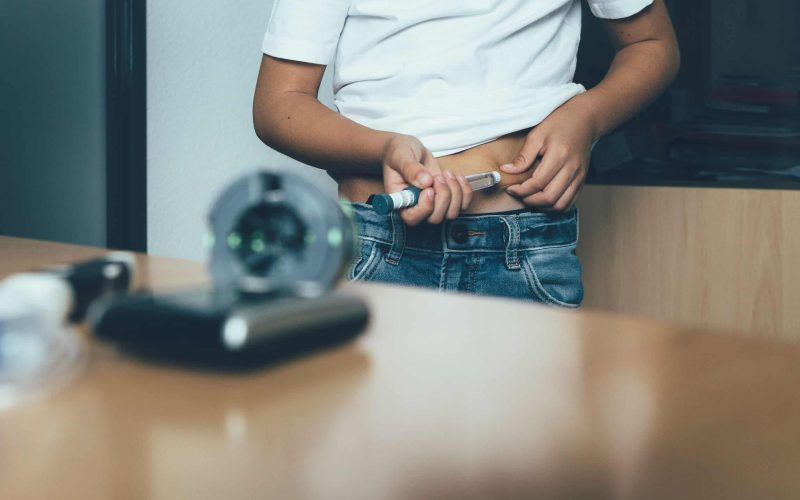 Cropped view of the abdomen of a diabetic child is injecting insulin with an insulin pen in the doctor office. Child diabetes concept